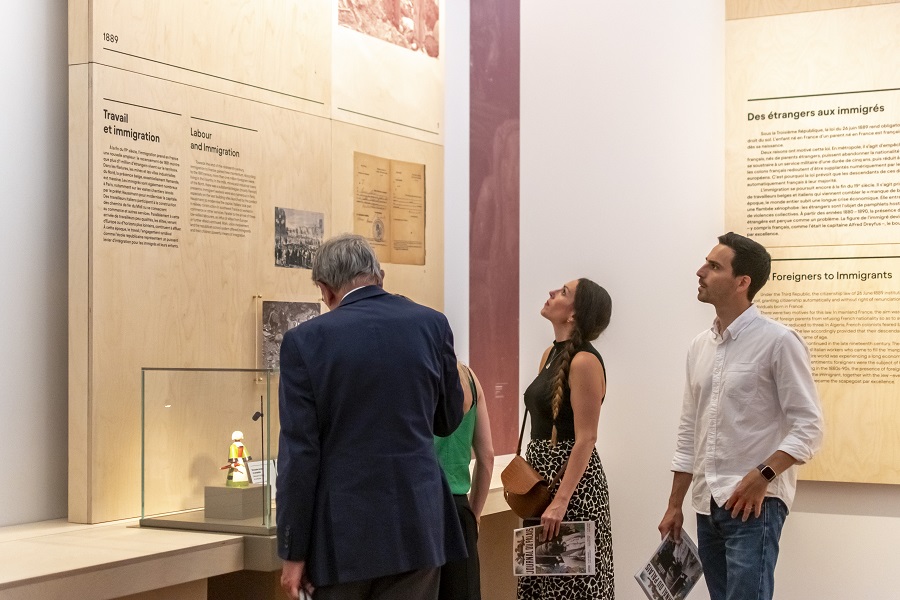 Quatre personnes sont debout en train de lire des explications lors de leur visite du Musée de l'histoire de l'immigration